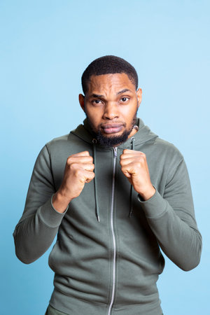 Active athletic african american guy clenching his fists on camera, doing warmup exercises before his boxing match in studio. Cheerful strong man with muscular build shows his power.の写真素材
