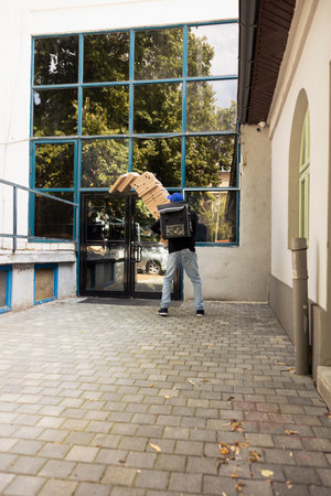 Clumsy pizza delivery man stumbles with massive stack of pizza boxes, dropping them at the customer doorstep. Shocked female client watches as the food order falls in a messy accident.の写真素材