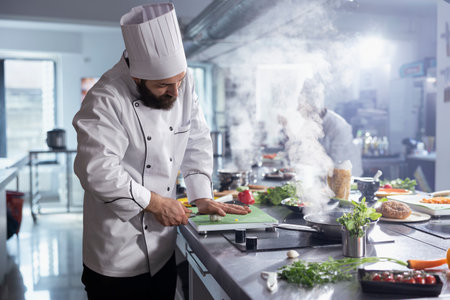 Young male head chef making crushed garlic on the cutting board, pressing the cloves to use condiments for a gourmet dish in the restaurant kitchen. Professional cook uses spices at counter.の写真素材