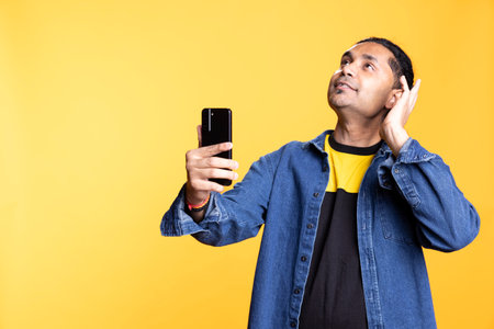 Joyous Indian man greeting people over online videocall on his phone, doing friendly gesture and chatting with friend. Excited young man bonding with someone using mobile phone webcam.の写真素材