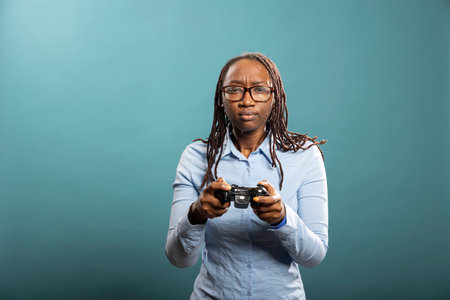 Young black woman holding modern controller, playing video games with focused expression. Serious...