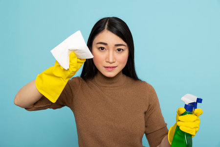 Portrait of asian housekeeper in yellow rubber gloves holding detergent spray bottle and paper...