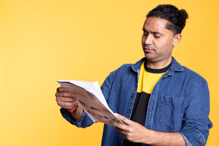 Indian accountant doing profit analysis for company and browsing files, standing against orange background. Worker doing financial budgeting and forecasting, looking over paperwork graphs.の写真素材
