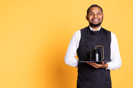 Restaurant worker serving people with tea before their dinner order, bringing the teapot at the table for professionalism. Waiter serves clients for satisfaction, service oriented industry.の写真素材