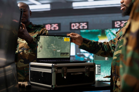 Military officer conducts tactical reconnaissance in command room, utilizing laptop for data analysis. Army expert uses satellite technology on notebook to look at aerial map, pinpointing targetsの写真素材