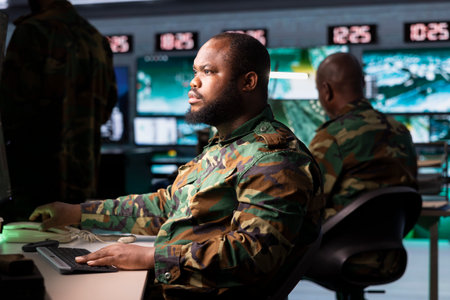 Military early warning systems operator in control room monitoring incoming enemy aerial attacks. African american army agent maintains air space superiority with radar during armed conflictの写真素材