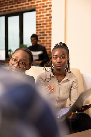 Selective focus on professional women attentively listening to coworker during meeting in startup office. African american female hr staff, evaluating and discussing performance metrics of employee.の写真素材