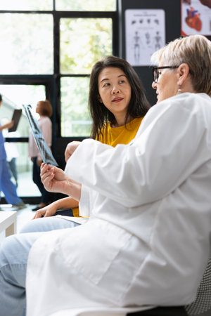 Inside a hospital lobby, medic does radiography scan interpretation with asian woman during checkup....