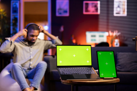 Young black person enjoys music on wireless headset next to isolated display, feeling happy and casual laying on the bean bag in the living room. Relaxed chill man in his trendy loft.の写真素材
