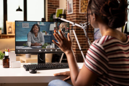 Black woman working remotely, attends group video conference on desktop pc in cozy home office. Professional remote manager speaking to colleagues during online business meeting using computer.の写真素材