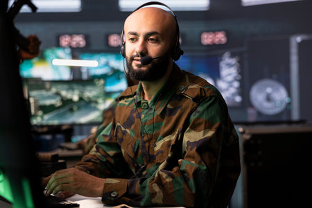 Agent in command room uses military tech to identify threats from enemies. Army operator in base of operations uses headset mic to communicate information to generals on war front lineの写真素材