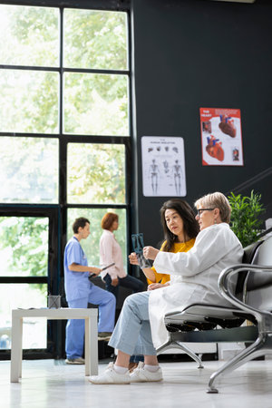 Physician helping asian woman interpret X ray images after a recent scan. Modern hospital staff supporting people with illness, provide recovery plan and supportive medical care.の写真素材