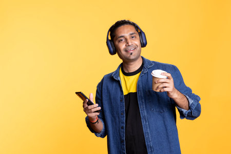 Funky person having fun with headset and dancing on oriental rhythm, enjoying poses in the studio. Upbeat thrilled guy entertaining himself doing groovy cool movements and swinging arms.の写真素材