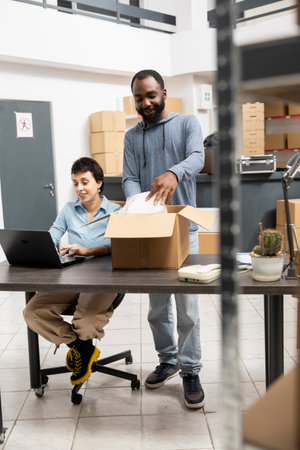 Two depot employees managing custom orders and hand packing goods in a supply room warehouse. Overseeing small business logistics and merchandise for distribution, import export.の写真素材