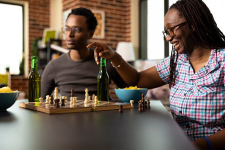 Cheerful black woman playing chess, smiling with excitement as she moves a piece, anticipating win....