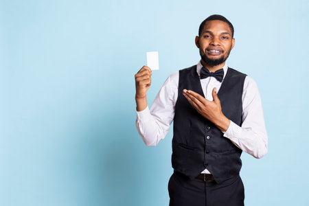 Classy hotel bellboy in tuxedo giving the room access key card to guest after check in, offering...