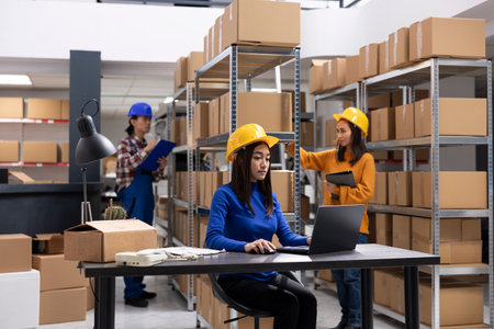 Asian staff member in a local brand supply room prepares products and taped boxes for shipment. Small business activity uses in house logistics for storage and delivery services.の写真素材