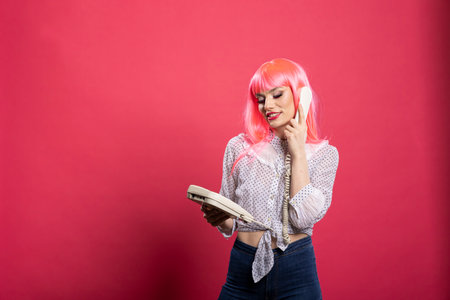 Cheerful woman with pink hair using landline, smiling and enjoying pleasant conversation. Young...