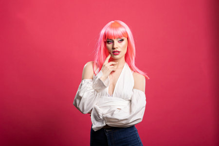 Stylish pretty woman with hand on chin, radiating confidence and charm in studio photoshoot. Gorgeous model wearing fashionable outfit, poses casually with hand on face against pink background.の写真素材