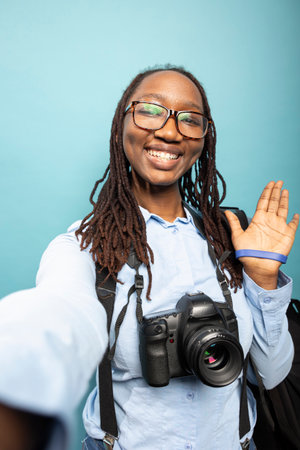 African american woman waving towards camera with bright smile, recording personal vlog. Black...