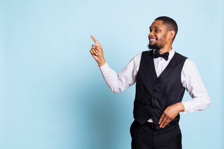 Doorkeeper bellhop pointing at something to left or right sides, indicating the direction for multiple amenities at the five star resort. Bellboy staff wearing a tuxedo uniform at his job.の写真素材