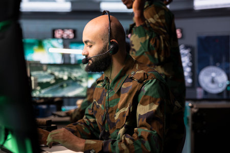 Army dispatcher looking at surveillance transmission on monitors, relaying data to troops using...