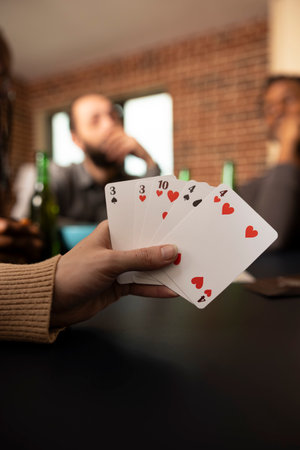 Selective focus on cards held by caucasian individual during casual game night with friends at home....