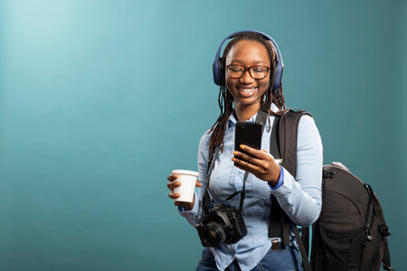 African American photographer with camera and backpack, listening to music, holding her coffee and...