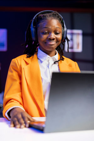 Woman wearing headphones at home using laptop to watch films on streaming services. Person using...