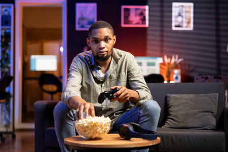 Online gamer enjoying shooter gaming competition with popcorn at home, participating in multiplayer...