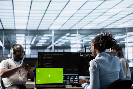 Green screen laptop in data center in front of IT support specialists working together, supervising...