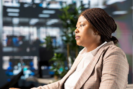 Confident businesswoman at her office desk working on report writing and answering emails, administrative tasks management. Black female expert reviewing objectives to ensure success.の写真素材