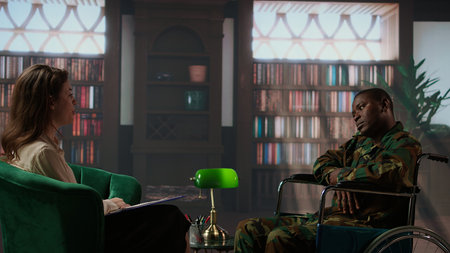 Wounded armed forces veteran in wheelchair discussing about war scenes, tells stories about horror of the combat. Distressed soldier with disability trying to recover with psychologist. Camera A.の写真素材