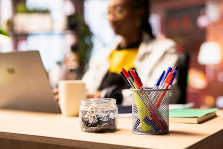 Focus on pens in desk organizer in front of remote worker typing on notebook keyboard. Close up of...