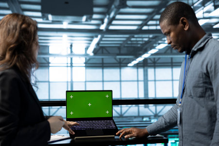 Admins using green screen laptop in data center, managing server virtualization. IT professionals...