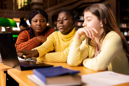 A professor assisting teen schoolgirls during tutoring session at the library, discussing about the...