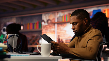 Startup entrepreneur in wheelchair using tablet to do research, looking to grow value of company. Venture business manager with disability using device, developing innovative growth strategy, camera Bの写真素材