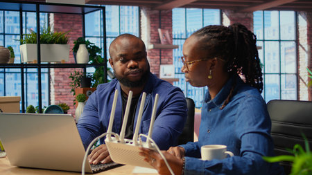 African American angry woman pulling out the LAN cable from the router while her partner reads a...