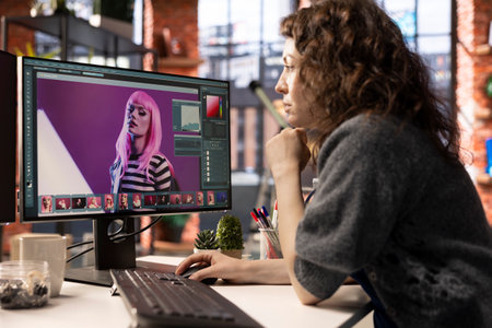 Female graphic designer editing photos on a modern computer setup in agency office, using an...