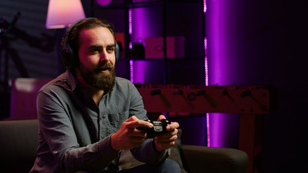 Smiling man putting headphones on to play videogames on gaming console with teammates. Happy player...