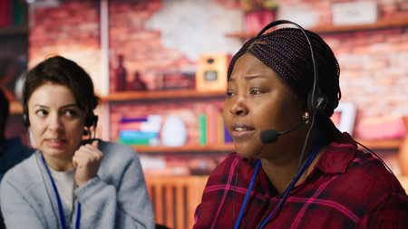 Customer center employee gesturing loud colleague to quiet down during conversation with client. Call center worker upset by noises in office while talking to customers using headphones mic, camera Aの写真素材