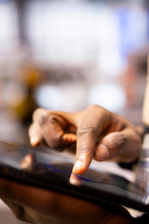 Industrial automation engineer configures robotic arms using CAD software on tablet. African American technician manages automated manufacturing systems through a digital interface.の写真素材