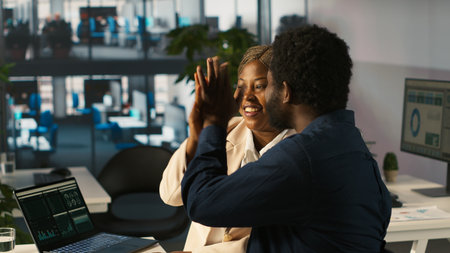 Coworkers doing high five in office after looking over positive revenue figures on PC. Happy employees congratulating each other, pleased by company economic boom, camera Aの写真素材