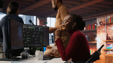 Programmer coding AI algorithm in startup, eating food at desk while refining machine learning models. Stressed woman using coding platform in Silicon Valley office and enjoying snack, camera Aの写真素材
