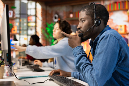 Call center employee dealing with upset customers, speaking with them using headset at office desk....