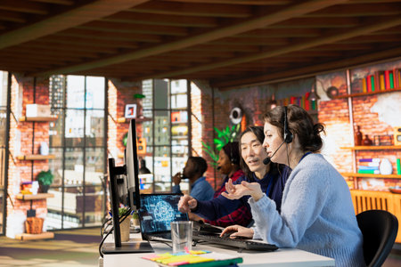 Experienced call center manager guiding intern on how to use AI chatbot in office. Asian customer...