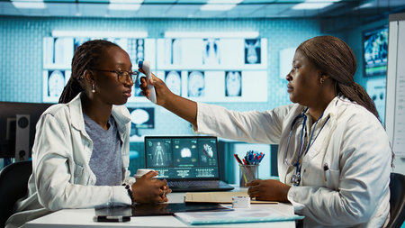 Black medic measuring the temperature during routine checkup at the clinic, using a digital...