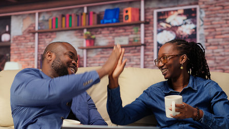 Black couple bonding on the couch unwinding with warm drinks after a long day. Smiling man and woman...