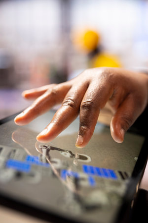 Industry 4.0 engineer programming robotic systems using a CAD software on tablet. African american automation technician utilizing a digital interface to manage smart manufacturing plant equipment.の写真素材