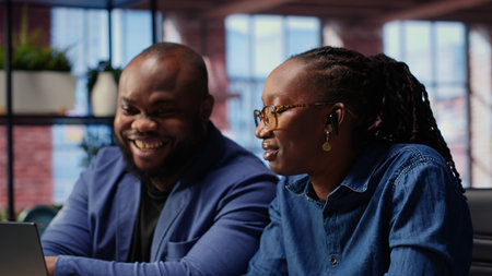 Black man and woman participating at a webinar remotely from home, listening to the online course with ear buds on laptop. Young couple freelancers using digital tools to develop their skills. Camera B.の写真素材